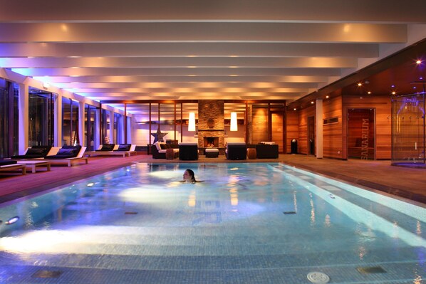Una piscina interior moderna con una persona nadando, sillas de descanso y un área de spa.