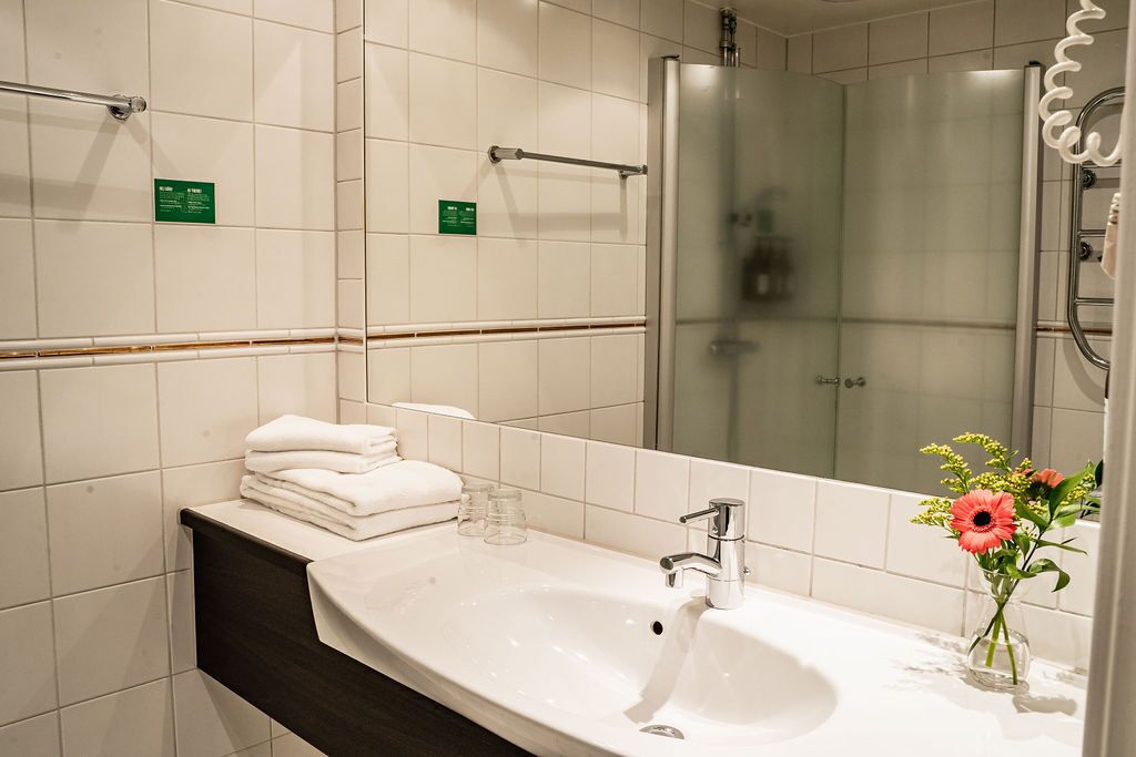 A modern bathroom with a large mirror, a white sink, and a glass shower enclosure.