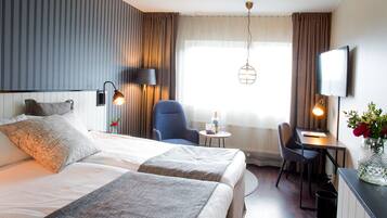 A hotel room with a large bed, two bedside tables, a desk with a chair, a small round table, and a TV.