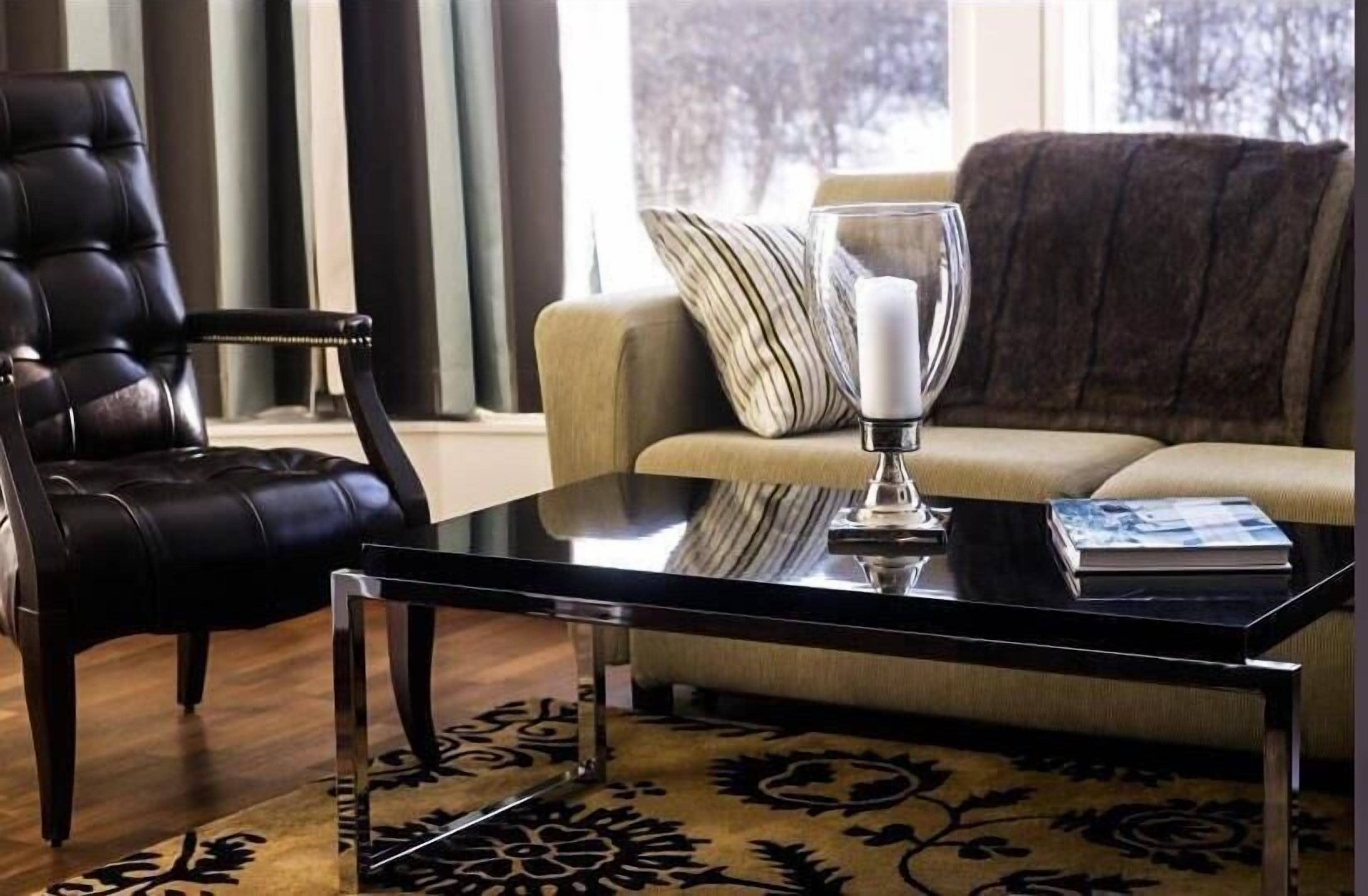 A living room with a leather chair, a sofa, a glass coffee table, and a patterned rug.
