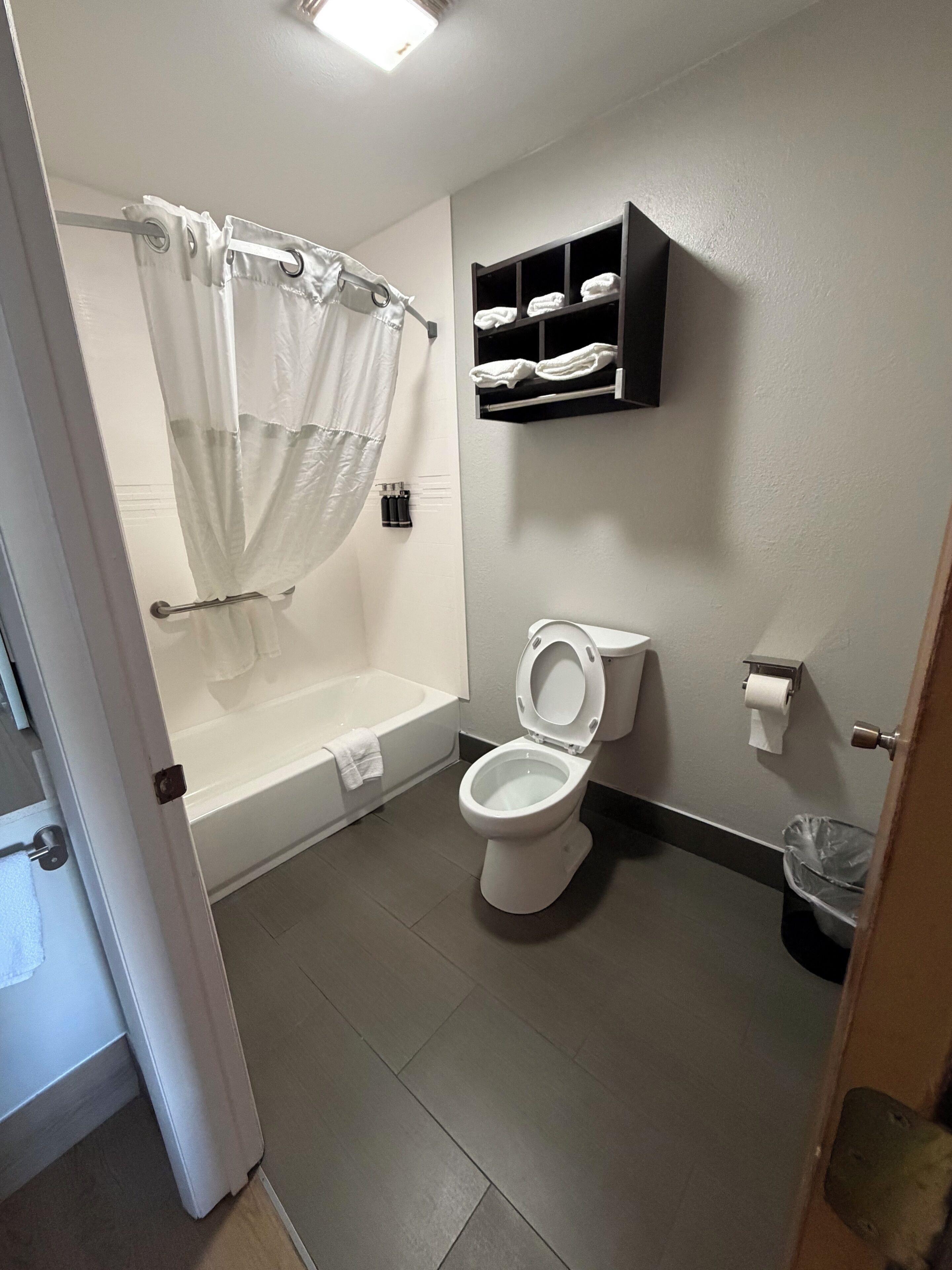 A bathroom with a bathtub, toilet, and a shelf with towels.