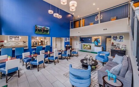 A hotel lobby with blue walls, a seating area with blue chairs, a bar, and artwork on the walls.