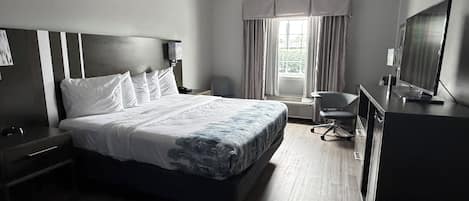 A hotel room with a bed, a desk, a chair, a television, and a window with curtains.