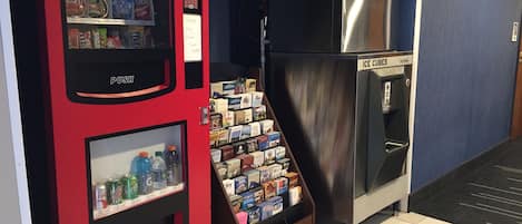 A vending machine with snacks and drinks, a refrigerator with ice cubes, and a display of books and magazines.