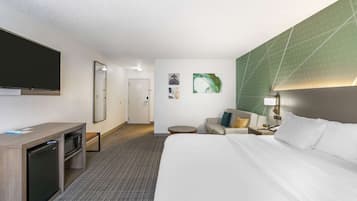 A hotel room with a bed, a desk with a microwave, a TV, a small table, and a chair.