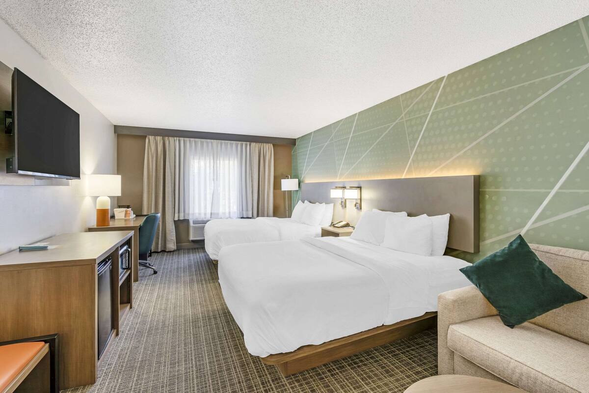 A hotel room with two beds, a desk, a TV, and a sofa.
