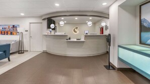 A reception area with a curved desk, a cityscape painting, a blue sofa, and a glass partition. - Comfort Inn & Suites Louisville Airport Fair & Expo (Louisville)