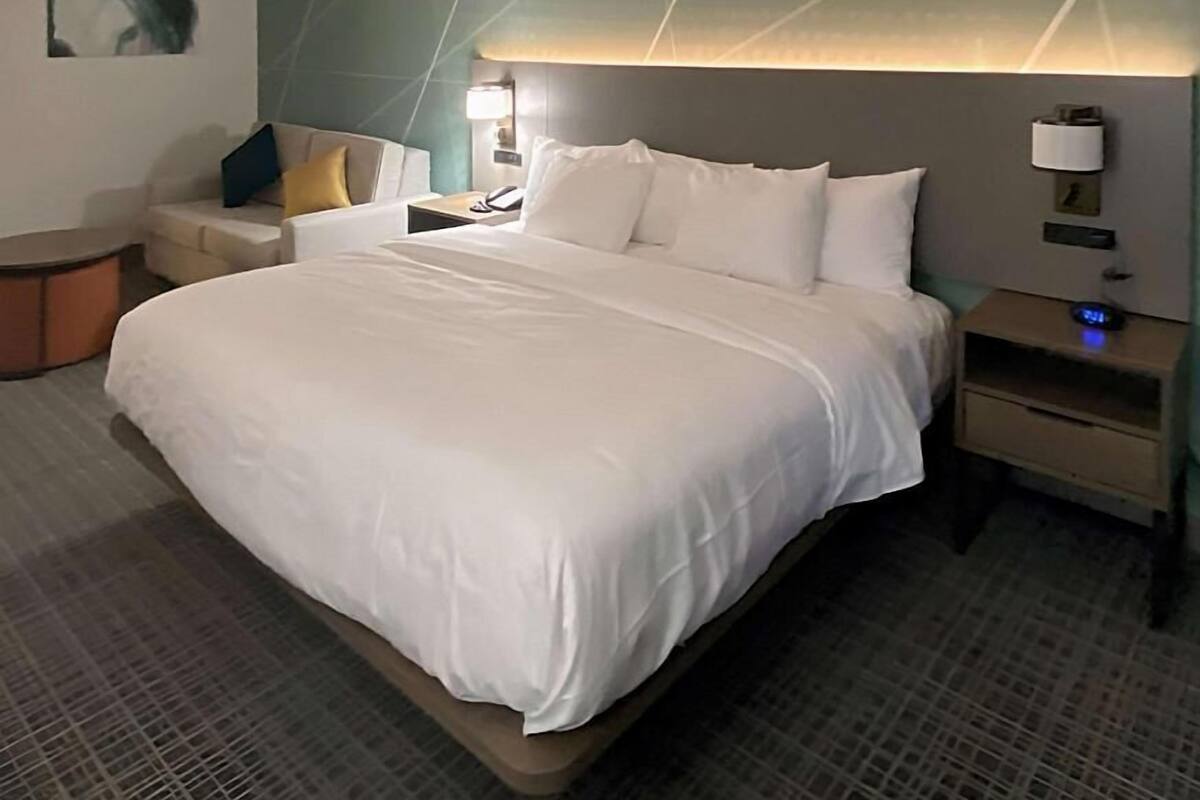 A hotel room with a large bed, bedside tables, a nightstand, a lamp, and a wall-mounted light fixture.