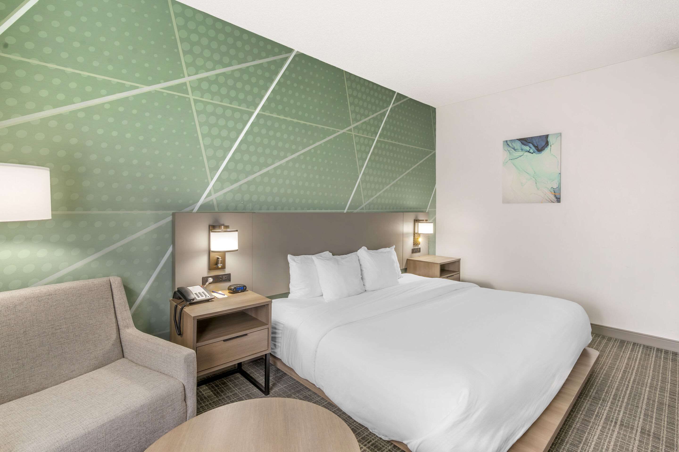 Habitación de hotel con una cama grande, un sofá, un escritorio con teléfono y una mesita.