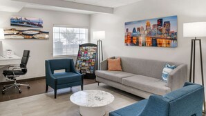 A modern waiting area with a grey sofa, blue armchairs, a coffee table, and a cityscape painting. - Comfort Inn & Suites Louisville Airport Fair & Expo (Louisville)