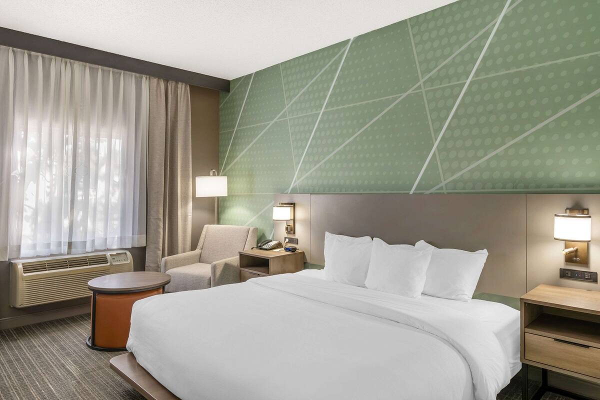 A hotel room with a large bed, a chair, a desk, and a lamp.
