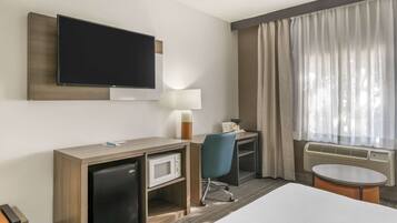 Habitación de hotel con cama, escritorio con computadora, televisor, microondas, lámpara y ventana con cortinas.