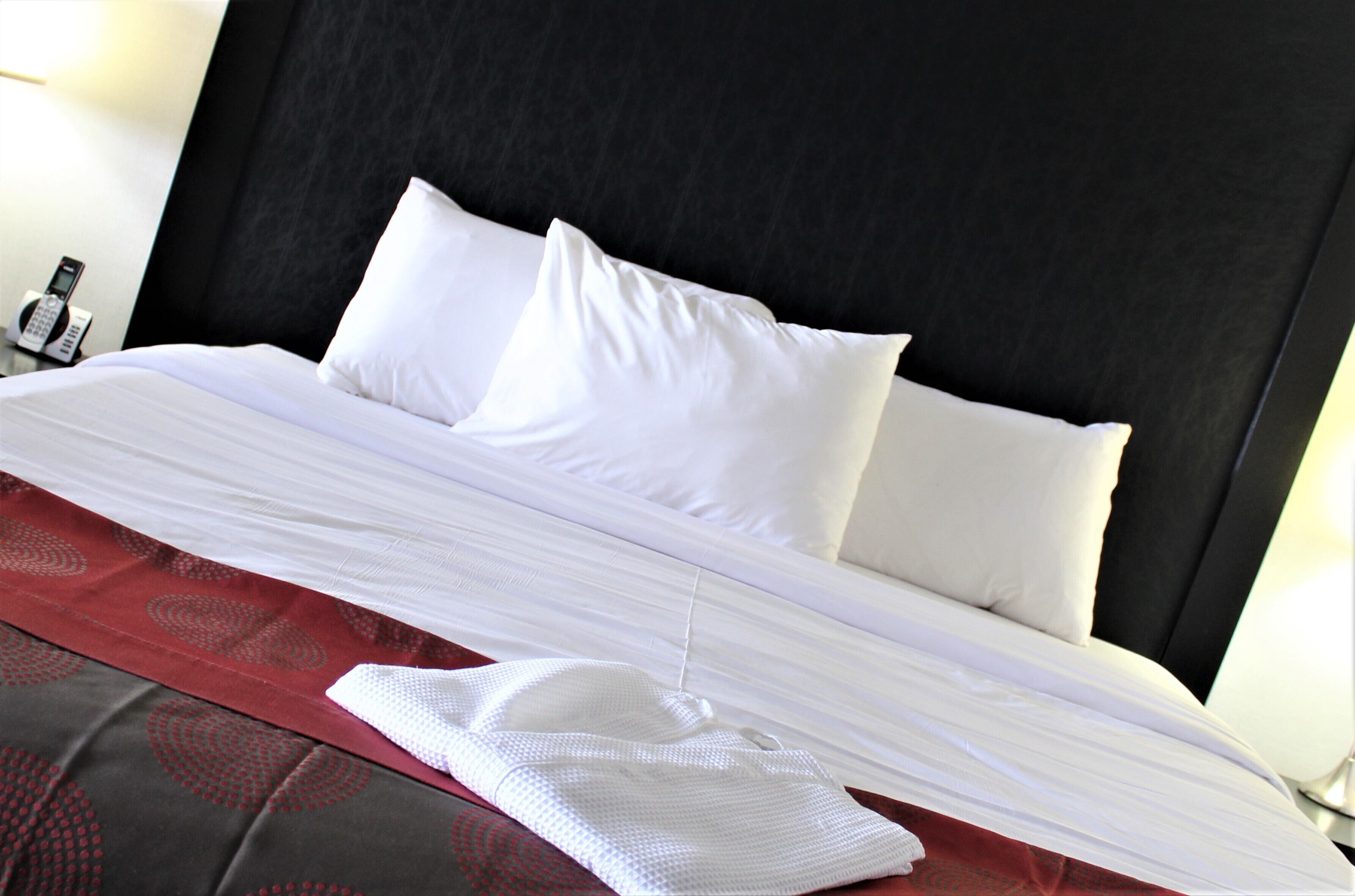 A neatly made bed with white linens and a red patterned bedspread.