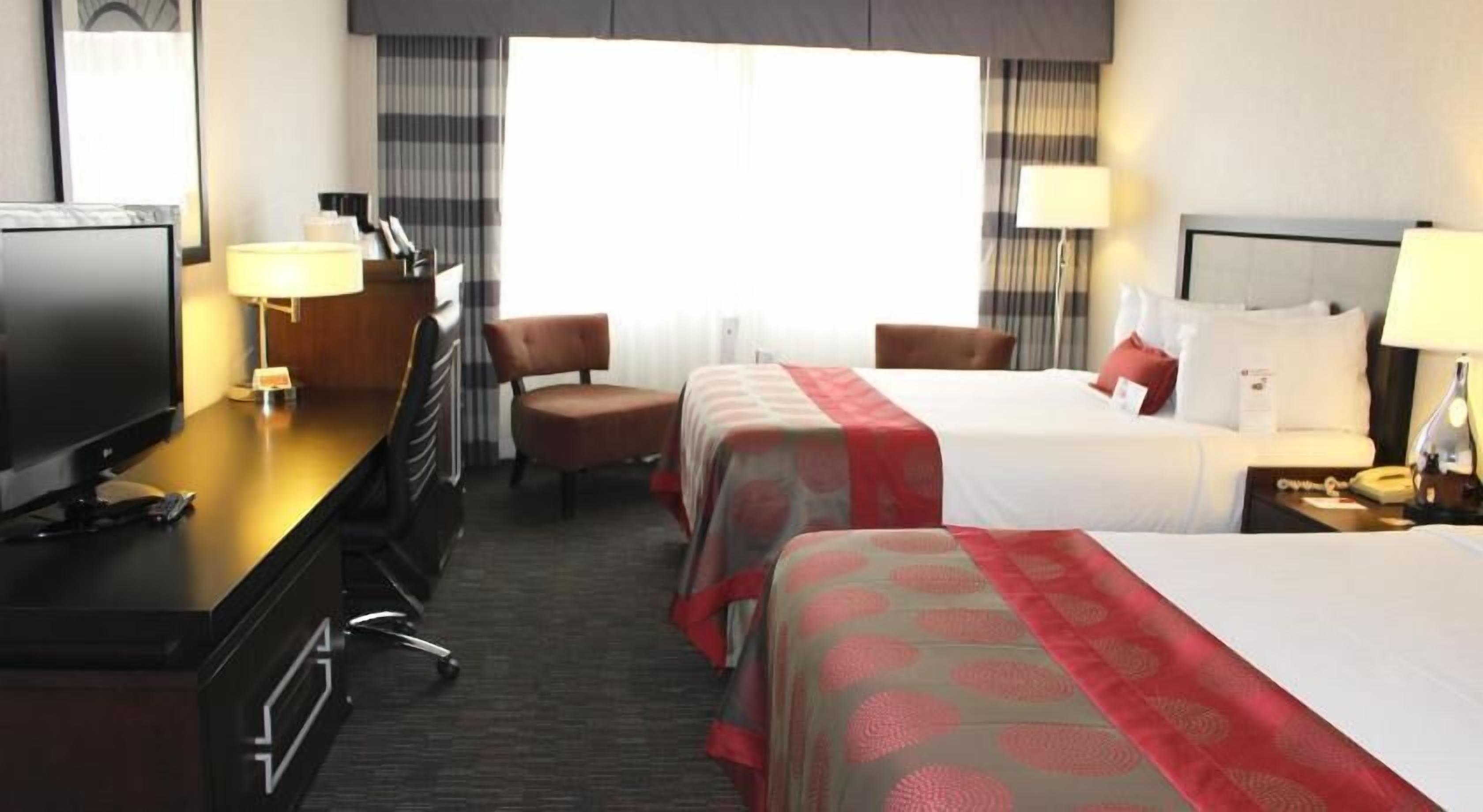 Une chambre d’hôtel avec deux lits, un bureau équipé d’une télévision, une chaise et une lampe de bureau.