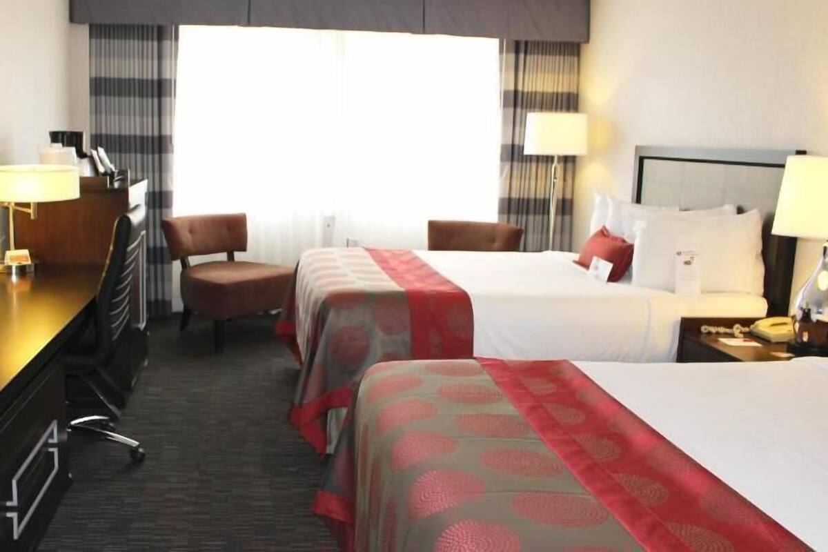 Une chambre d’hôtel avec deux lits, un bureau équipé d’une télévision, une chaise et une lampe de bureau.