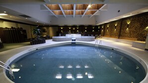 Une grande piscine intérieure dotée d’une fontaine centrale, entourée de fauteuils et d’un mur en pierre.