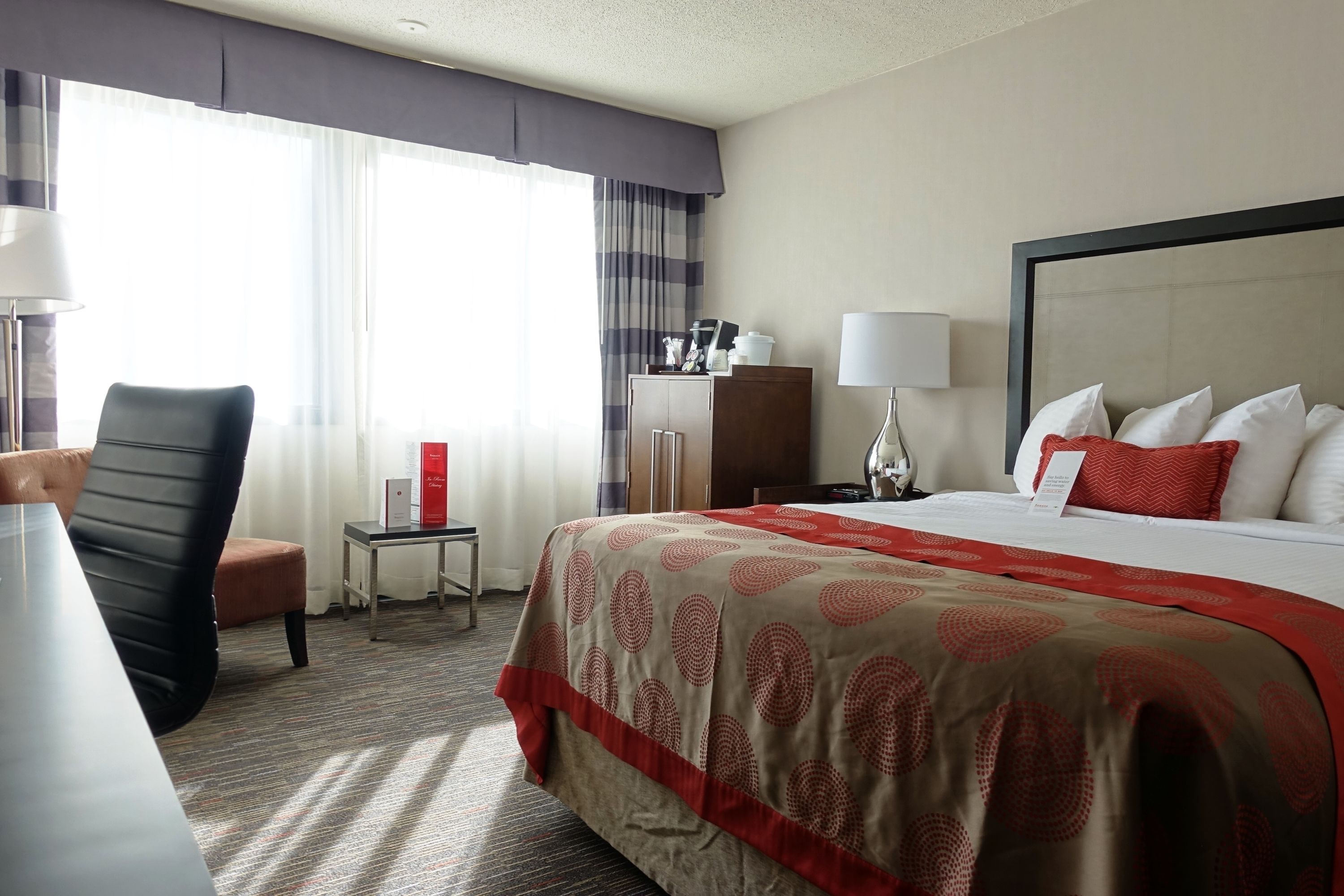Una habitación de hotel con una cama grande, un escritorio, una silla, una mesita y un armario.