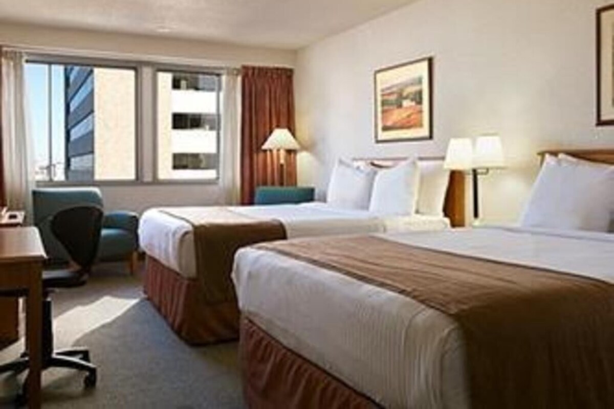Ein Hotelzimmer mit zwei Betten, einem Schreibtisch, einem Stuhl und einem Fenster mit Vorhängen.
