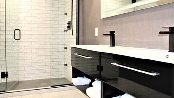 A modern bathroom with a glass-enclosed shower, a black vanity with a mirror, and white tiled walls.