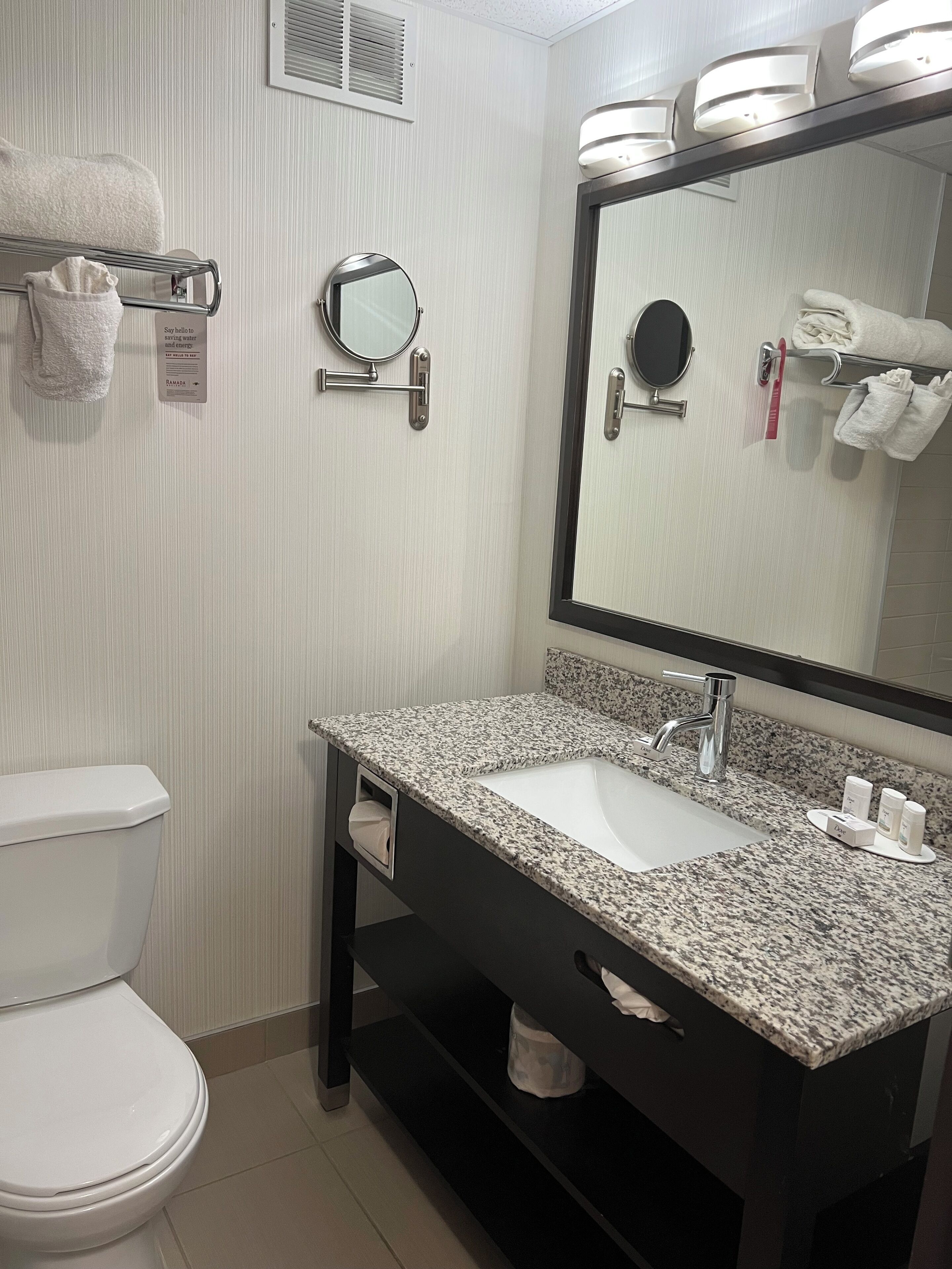 A bathroom with a white toilet, a granite sink, a large mirror, and a towel rack with folded towels.