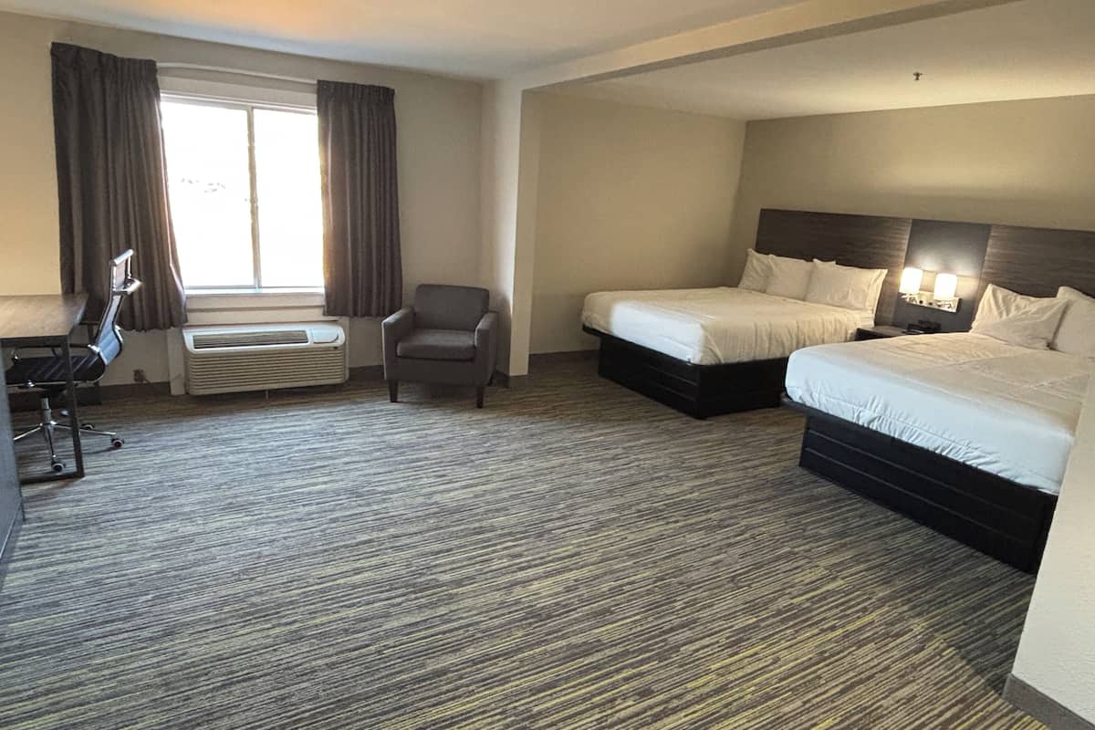 A hotel room with two beds, a desk, a chair, and a large window with curtains.