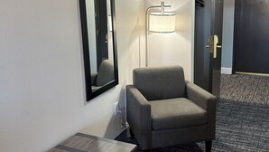 Een hotelkamer met een grijze fauteuil, een staande lamp, een spiegel en een deur.