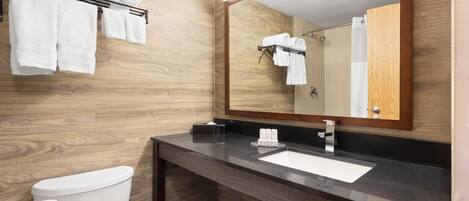 A modern bathroom with a wooden wall, a toilet, a sink with a mirror, and towels on a rack.