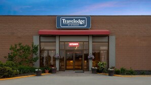 A Travelodge by Wyndham entrance with a brick facade, large glass doors, and potted plants.