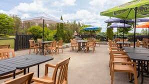 Un patio al aire libre con mesas, sillas, sombrillas y una estructura de piedra al fondo.
