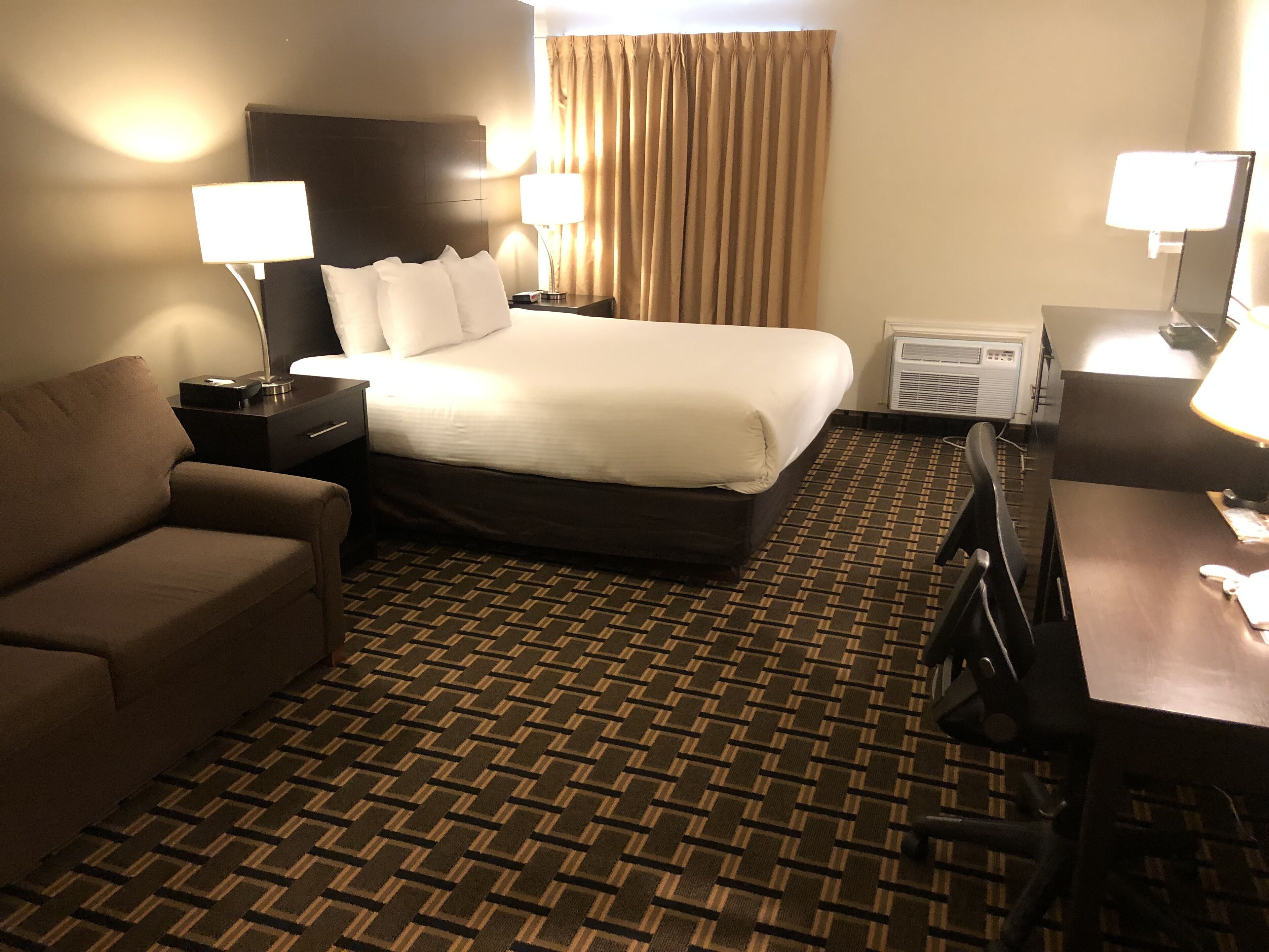 Una habitación de hotel con una cama, un sofá, un escritorio y dos lámparas.