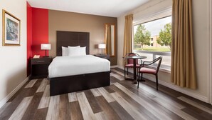 A hotel room with a large bed, bedside tables, a desk with a chair, and a view of the outdoors.