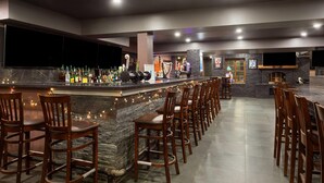 Una zona de bar con mostrador de piedra, varios taburetes altos y un televisor montado en la pared.
