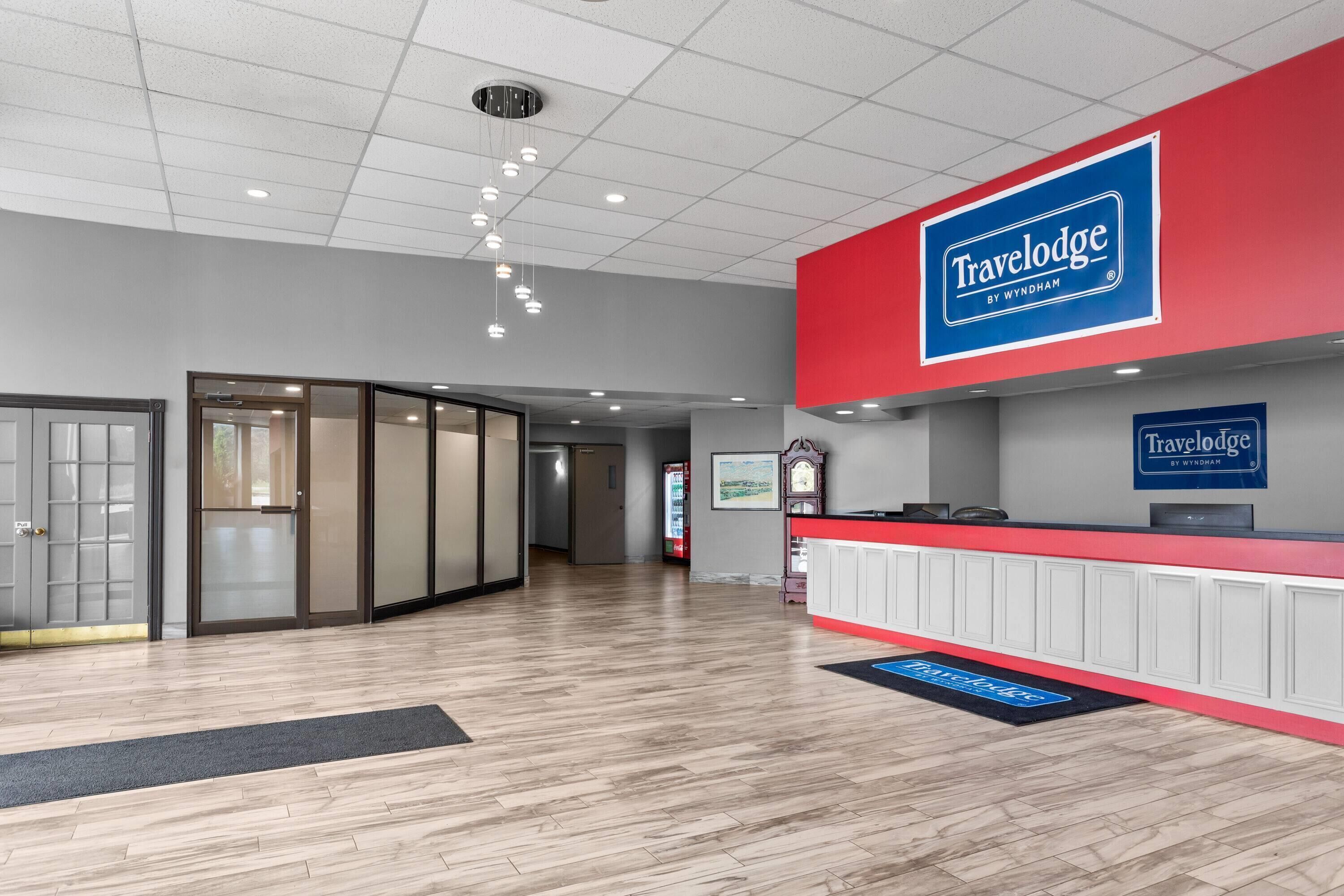 A reception area with a red and white color scheme, a 'Travelodge by Wyndham' sign, and a wooden floor.