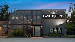 Un pub y restaurante llamado Castle John's con fachada de vidrio moderno y un letrero que indica su fundación en 2016.