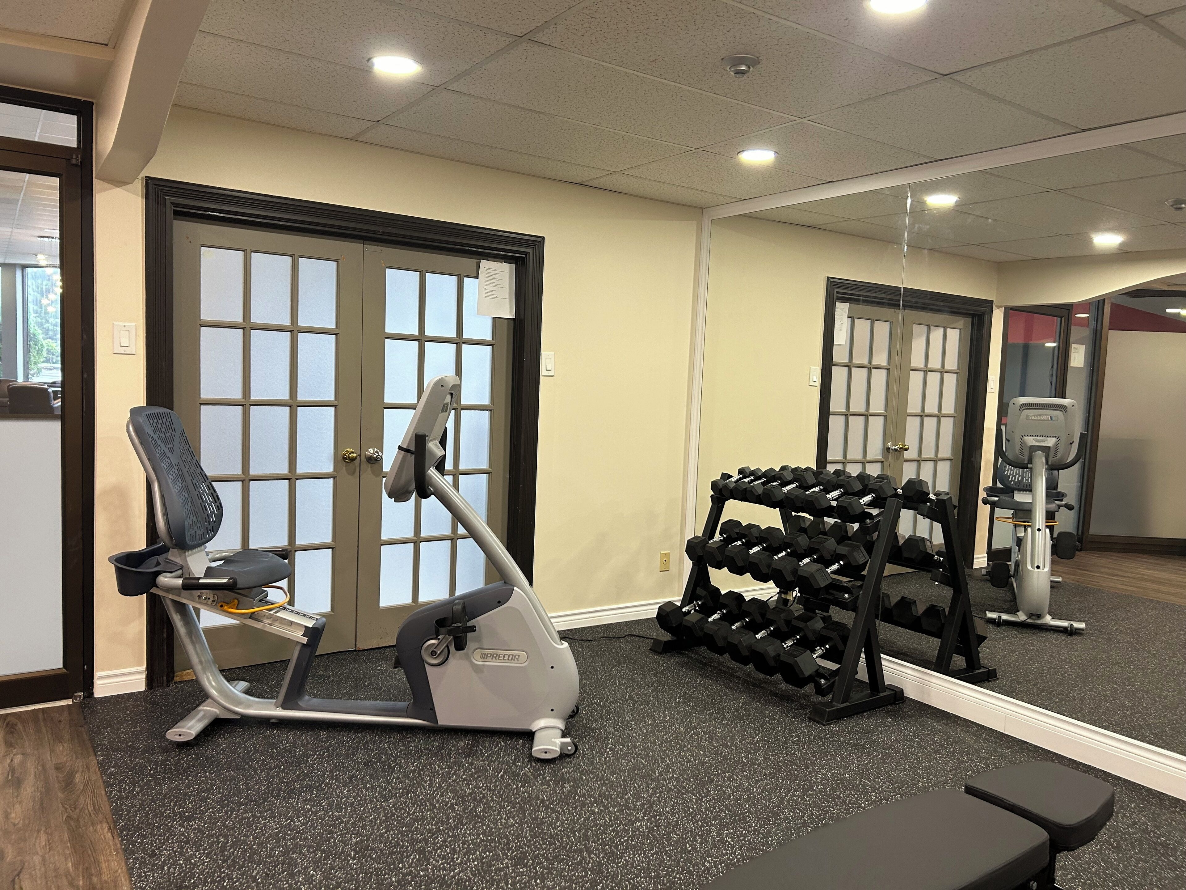 A gym with an elliptical machine, a bench, and a rack of dumbbells.