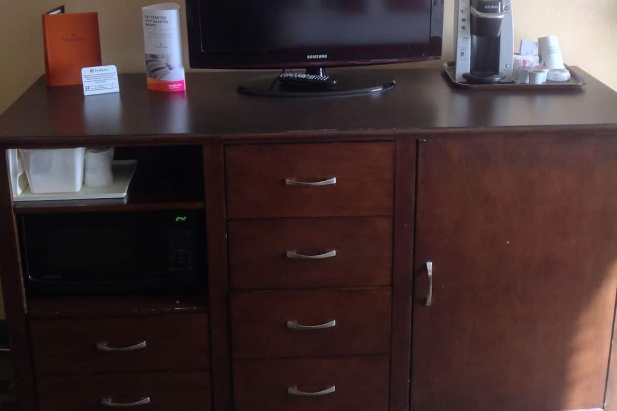 A wooden desk with a television, a coffee maker, and a microwave.
