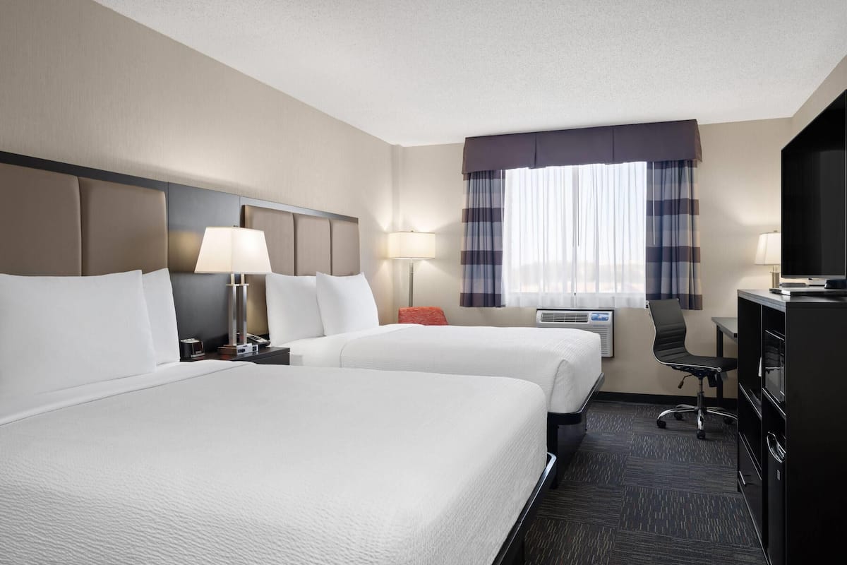 A hotel room with two beds, a desk, a chair, and a television.