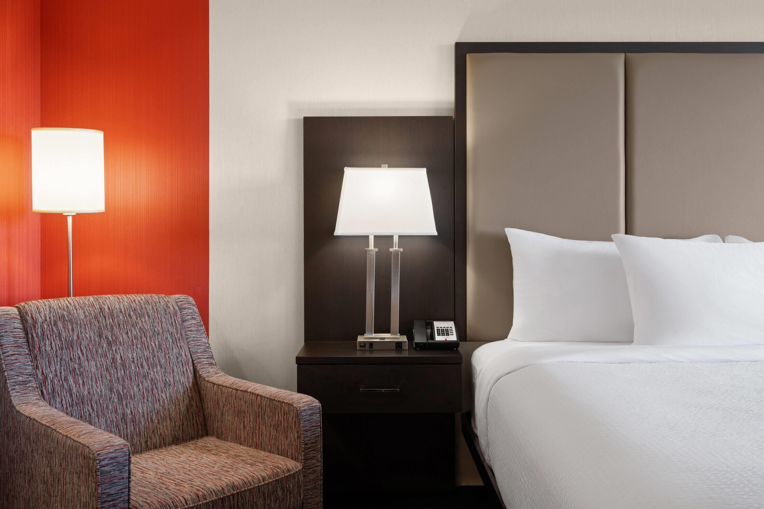 Une chambre d’hôtel avec un lit, une table de chevet avec une lampe, une chaise et un téléphone.