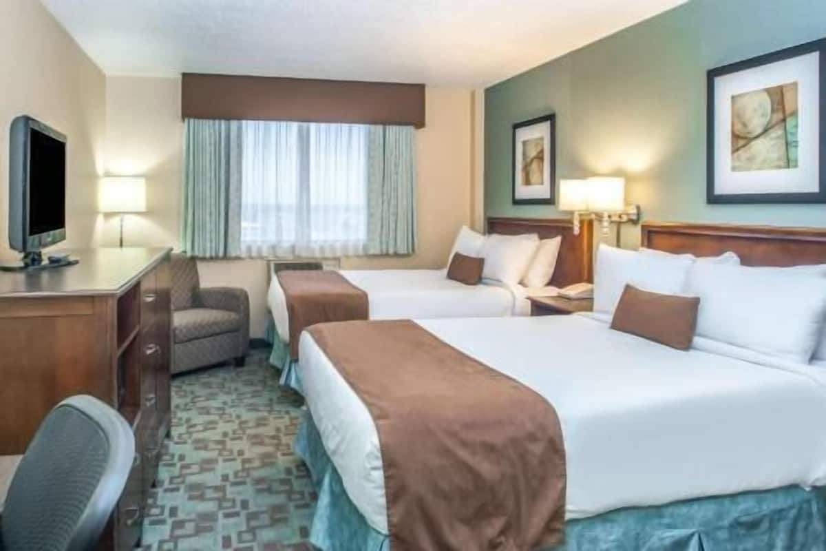 A hotel room with two beds, a desk, a chair, a television, and a window with curtains.