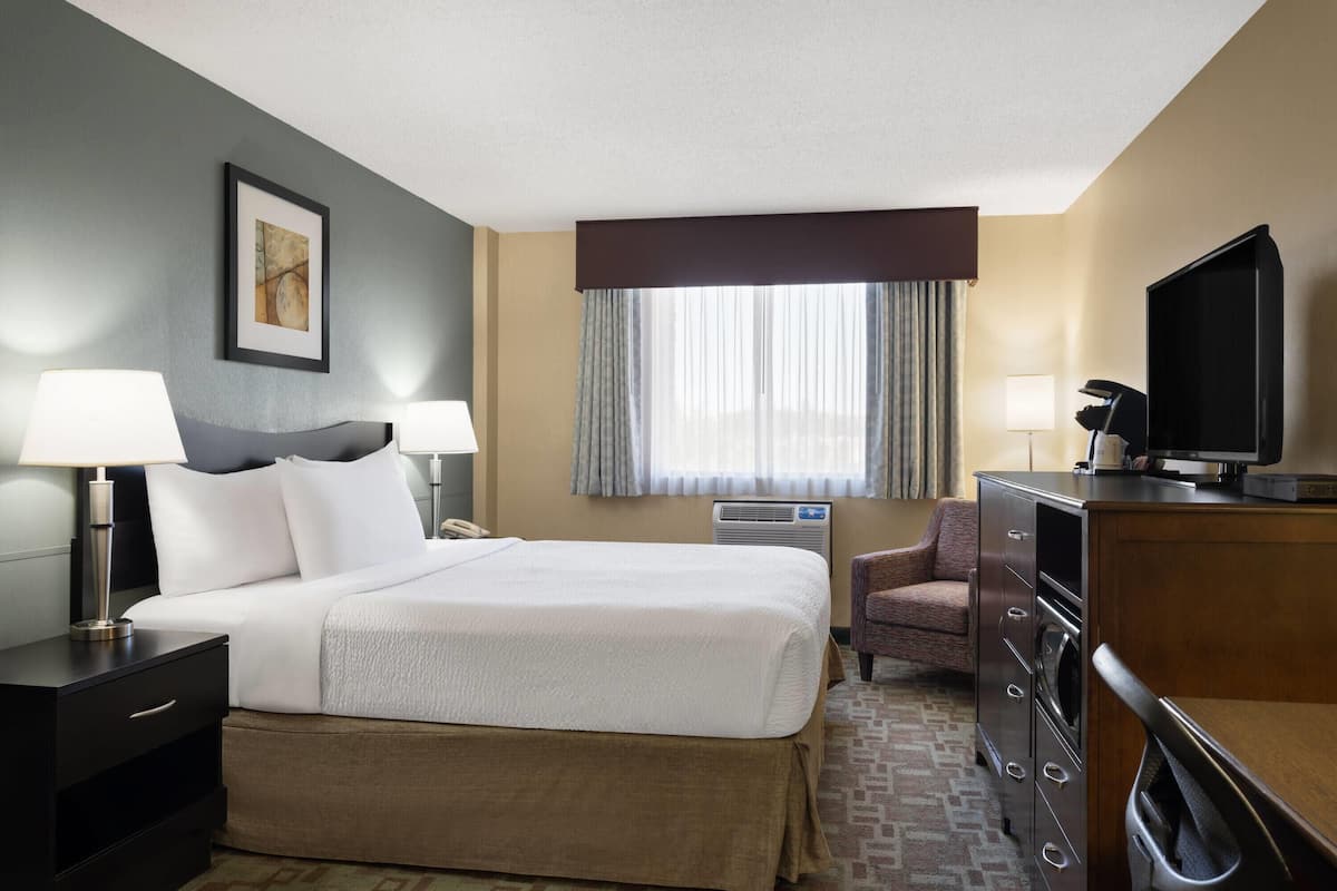 A hotel room with a large bed, two bedside tables with lamps, a television, a dresser, and a window with curtains.