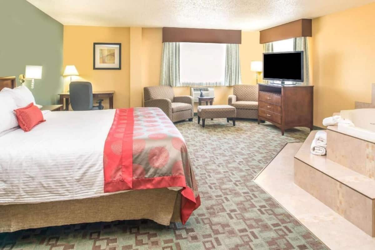 A hotel room with a bed, a desk, a chair, a TV, a sofa, and a bathtub.