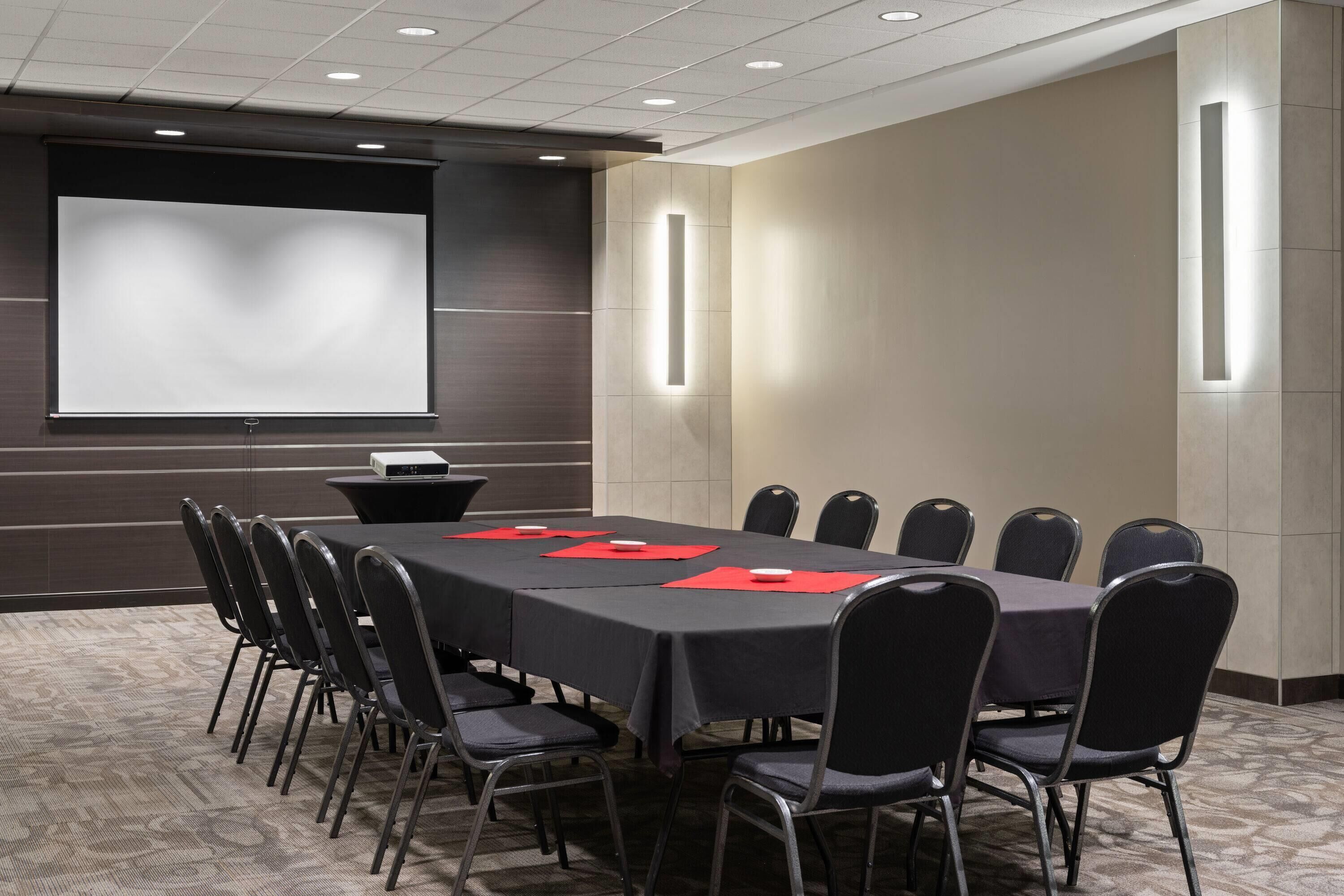 A conference room with a long table, black chairs, a projector screen, and a podium.