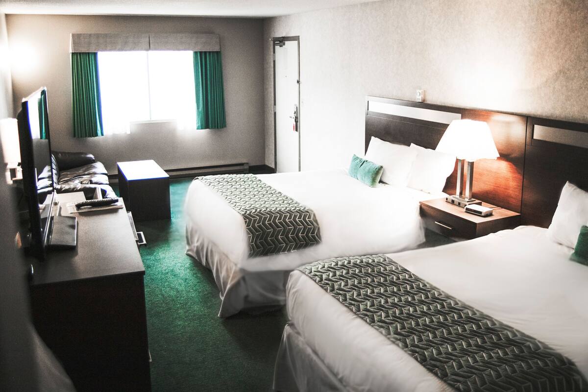 Habitación de hotel con dos camas, un escritorio, una silla, un televisor y una ventana con cortinas.