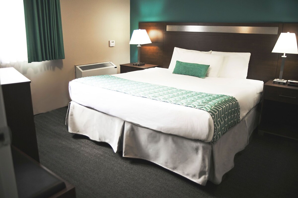 A hotel room with a bed, two bedside tables, a heater, and a window with curtains.