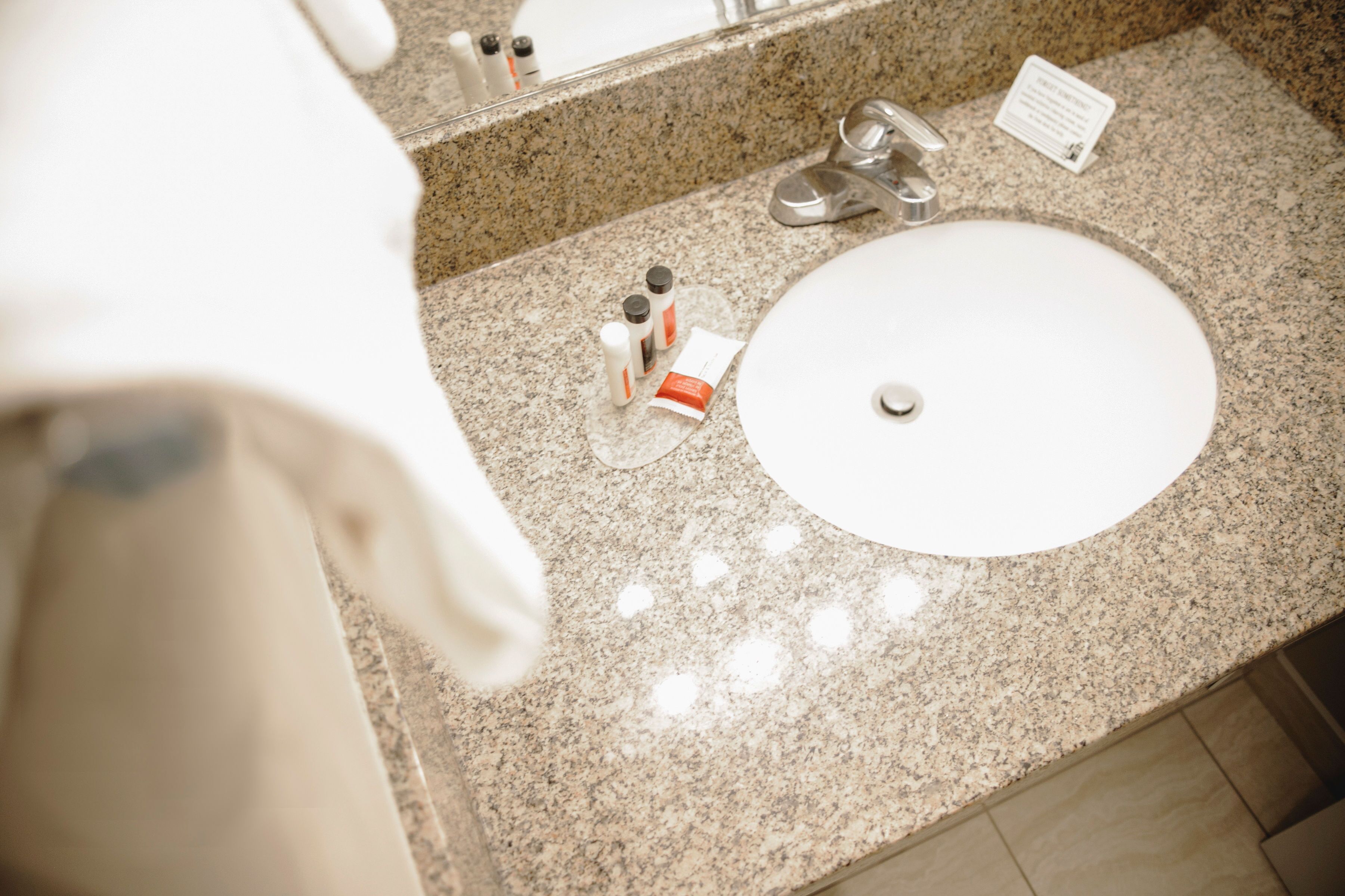 A bathroom sink with a granite countertop, a mirror, and toiletries.