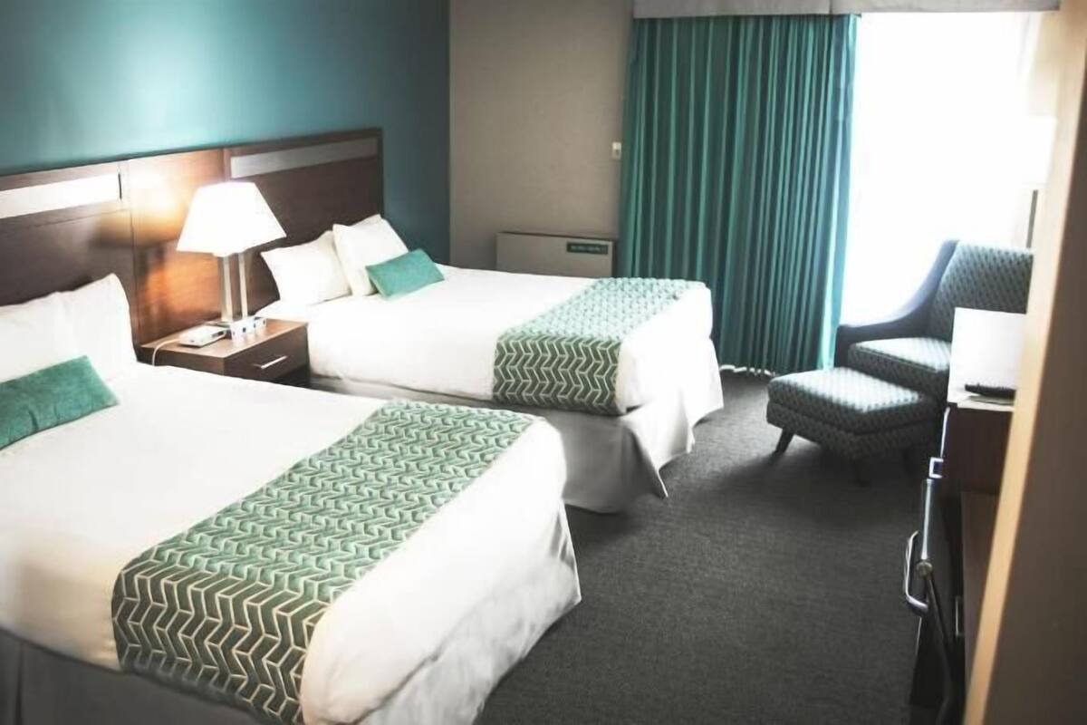Una habitación de hotel con dos camas, un escritorio, una silla y un ventanal con cortinas.