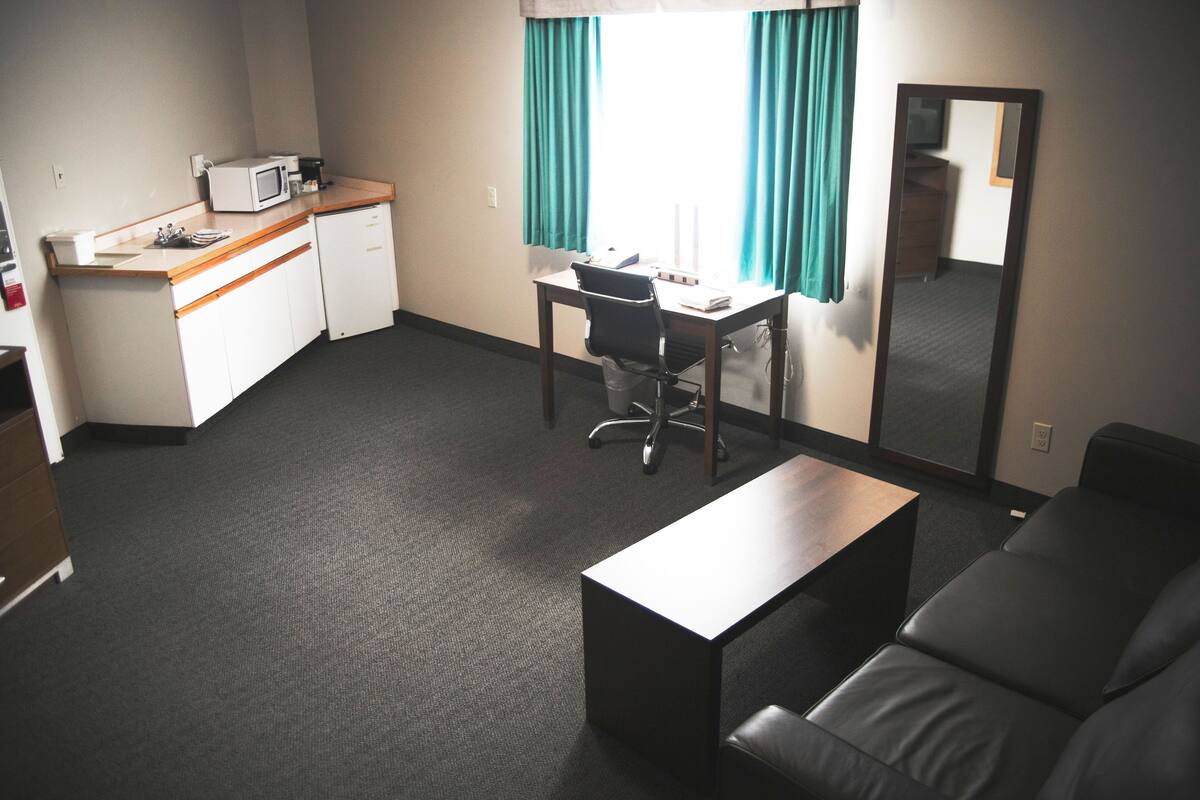 Una habitación de hotel pequeña con kitchenette, un escritorio, una silla, un sofá y un espejo grande.