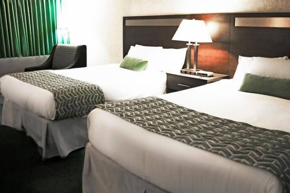 Una habitación de hotel con dos camas, una mesita de noche con lámpara y una silla.
