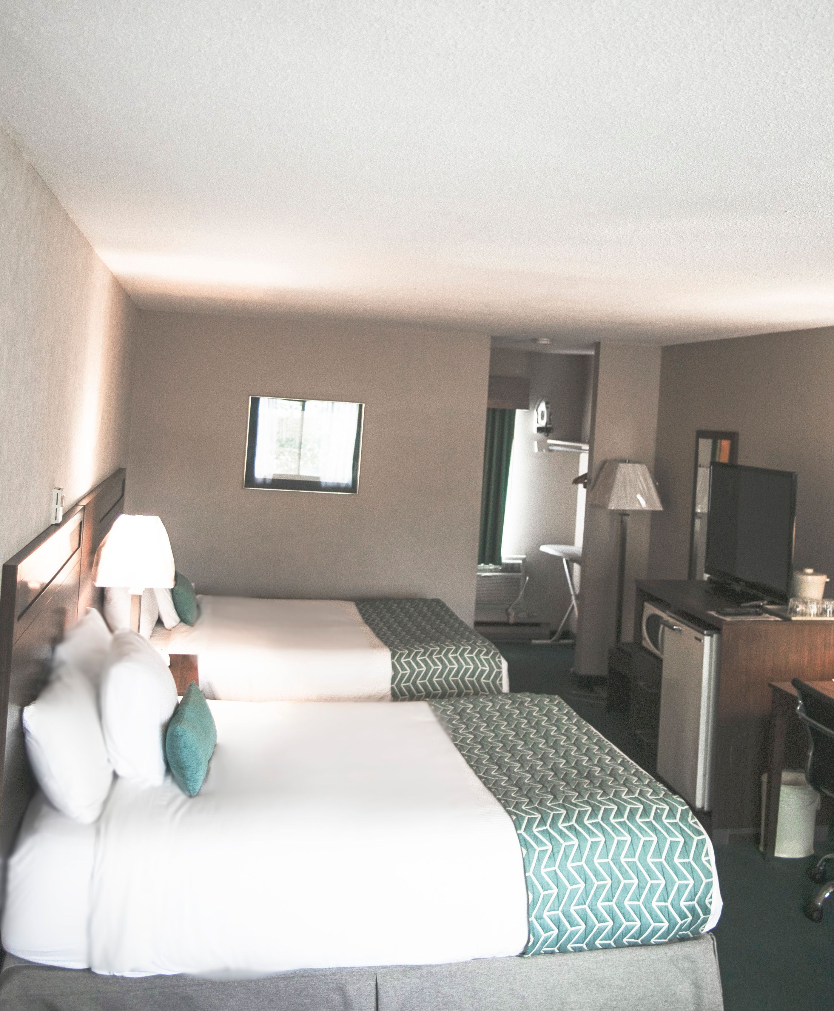 A hotel room with two beds, a desk, a chair, a television, and a window.