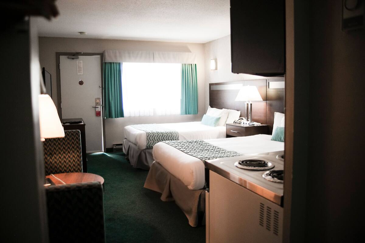 Una habitación de hotel con dos camas, un escritorio, una silla, una lámpara y una ventana con cortinas.